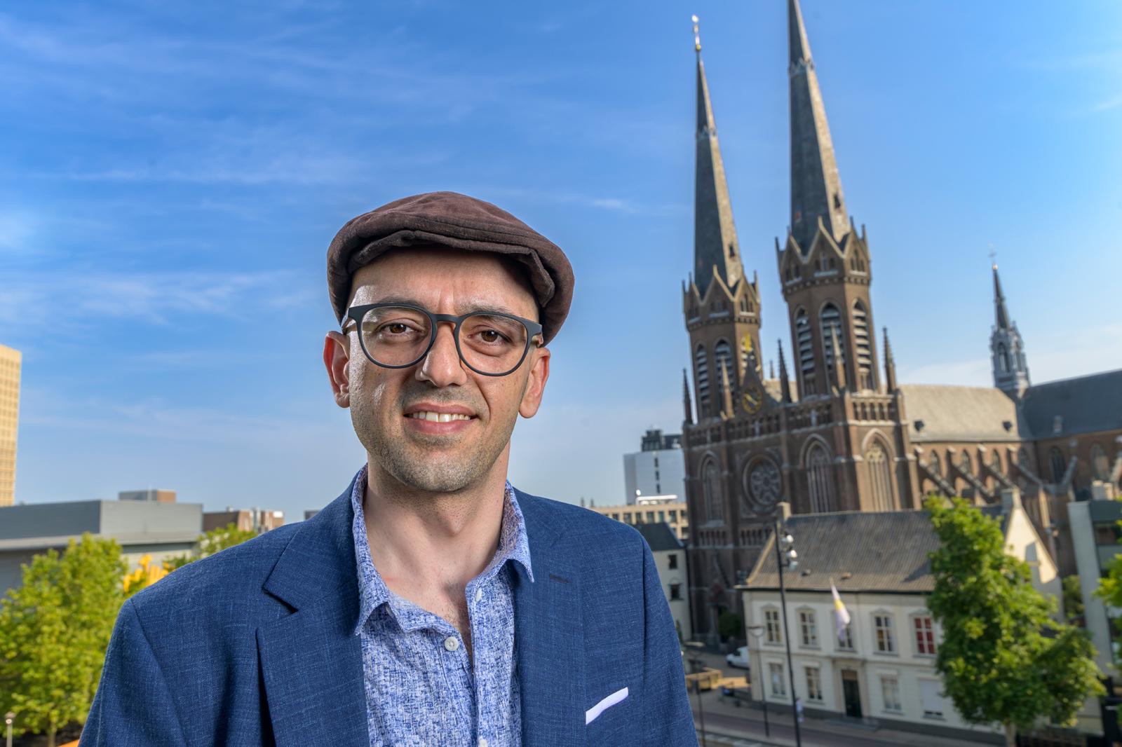 Kenan in blauw colbert met de Heuvelse kerk in Tilburg op de achtergrond